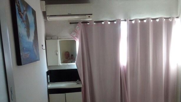 A bedroom with a bed, a desk with a mirror, an air conditioner, and a bathroom with a toilet. - Hotel pousada chic (Tatui)