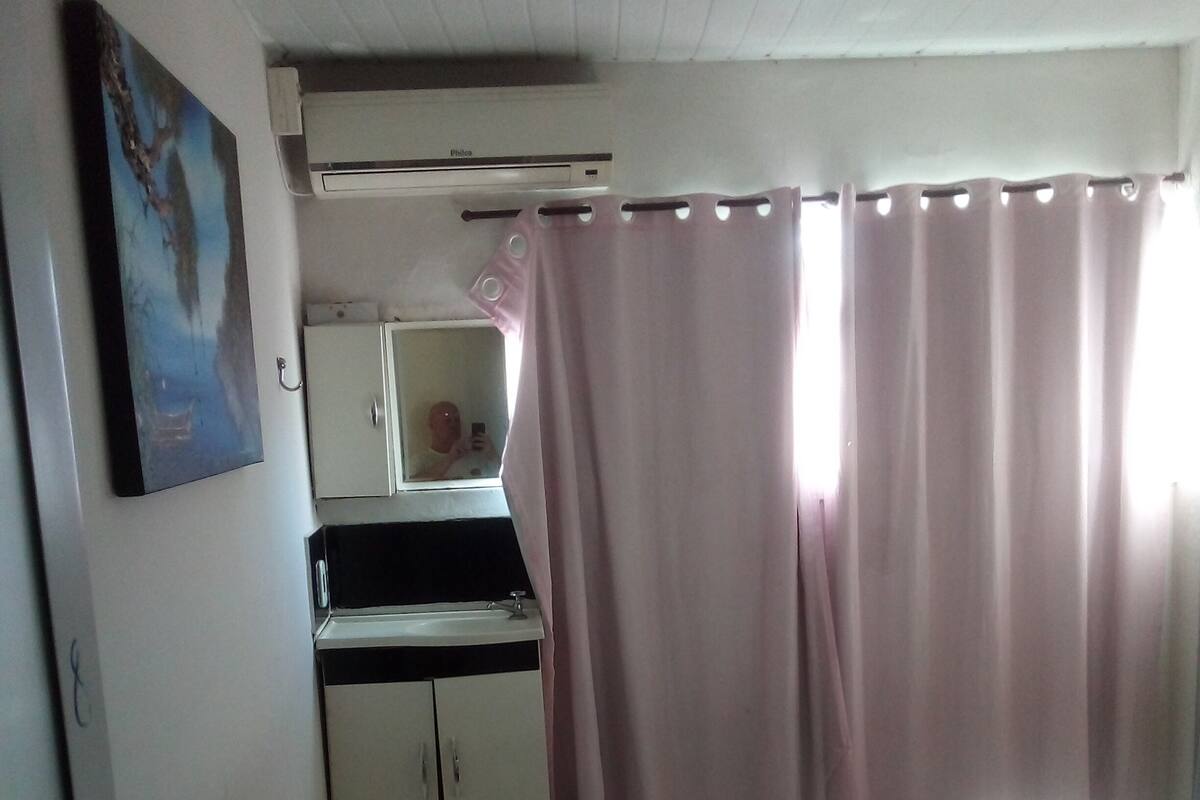 A bedroom with a bed, a desk with a mirror, an air conditioner, and a bathroom with a toilet.