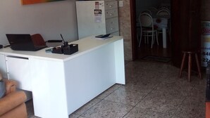 A reception desk with a computer, a phone, and a calendar. There are two chairs and a table in the background. - Hotel pousada chic (Tatui)