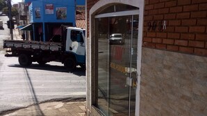 A hotel entrance with a glass door, a brick wall, and a tiled sidewalk. - Hotel pousada chic (Tatui)