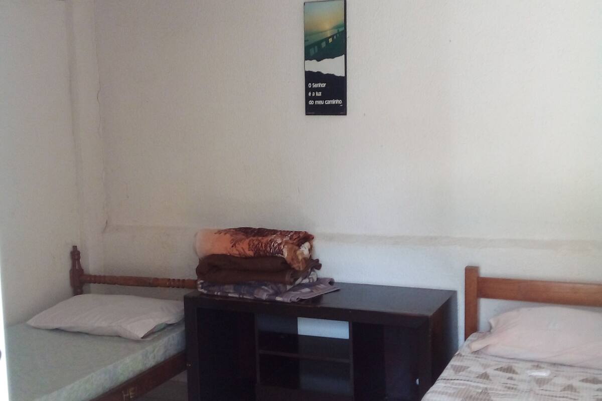 A small, simple room with two beds, a nightstand, and a wall-mounted poster.