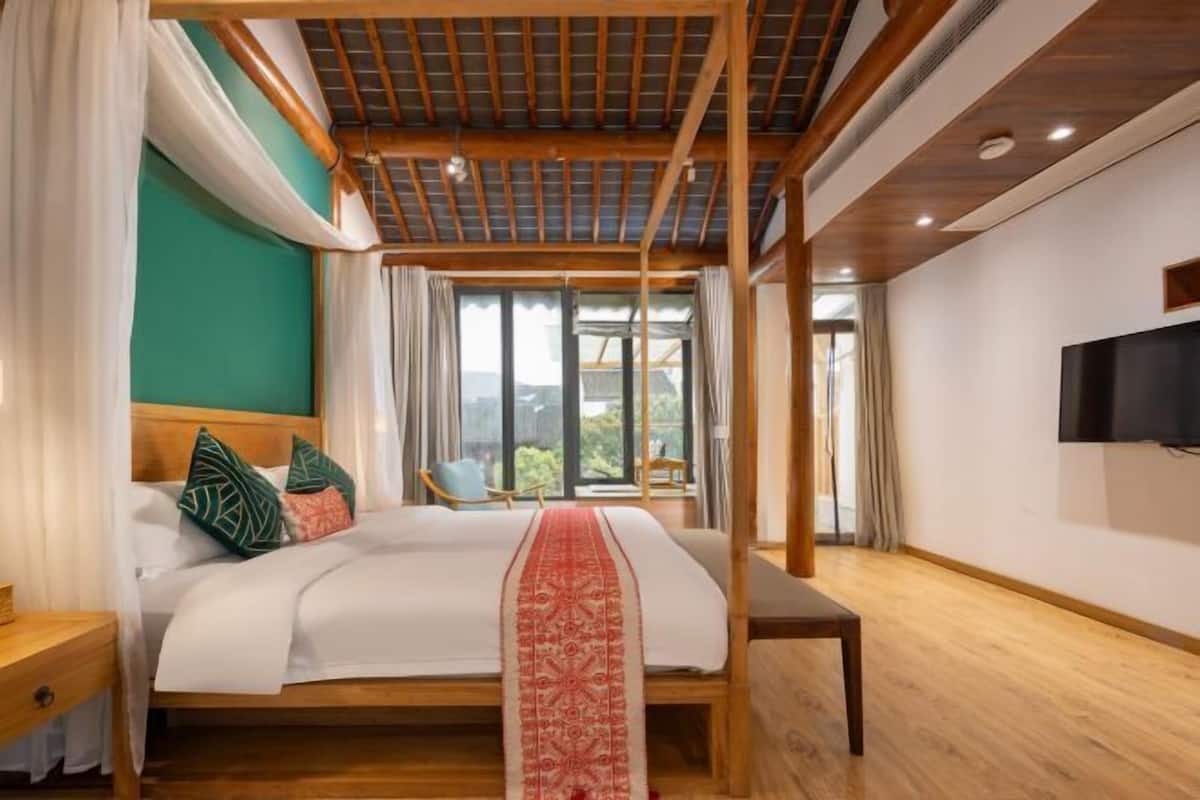 Une chambre avec un plafond en bois, un grand lit recouvert d’un couvre-lit rouge, un téléviseur fixé au mur et une fenêtre avec des rideaux.