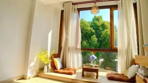 A modern living room with a large window, a sofa, a coffee table, and a vase with flowers. - Shuishangju Japanese Landscape Inn Suzhou Tongli (Suzhou)