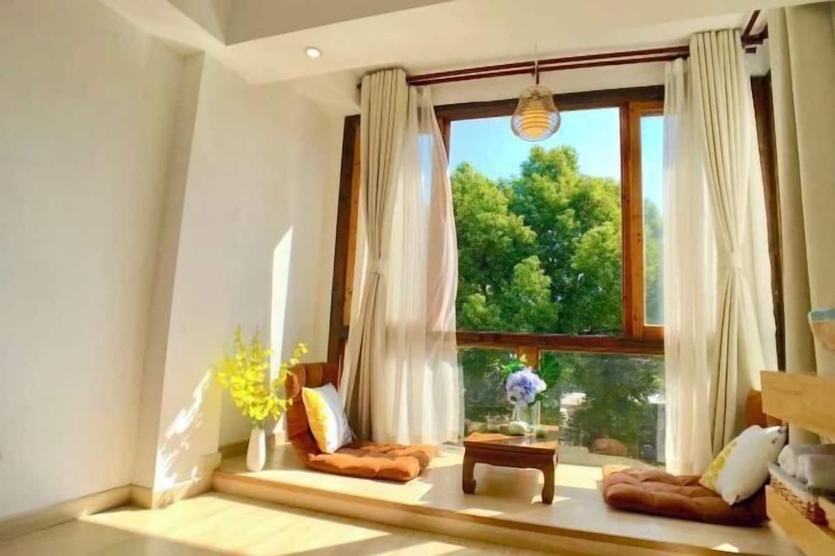 Un salon moderne avec une grande fenêtre, un canapé, une table basse et un vase rempli de fleurs.