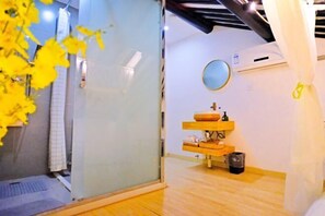 Un baño con cabina de ducha de vidrio, tocador de madera con espejo y un pequeño cubo de basura.