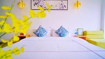 Habitación de hotel con una cama grande, dos almohadas, una mesita de noche y un sofá amarillo, además de una obra de arte colgada en la pared.