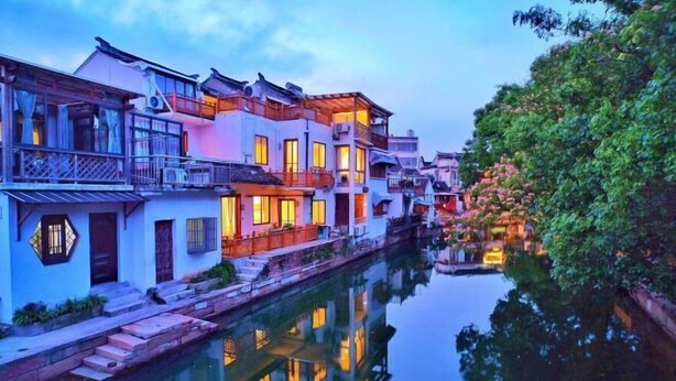 A canal-side building with multiple stories, balconies, and a reflection in the water. - Shuishangju Japanese Landscape Inn Suzhou Tongli (Suzhou)