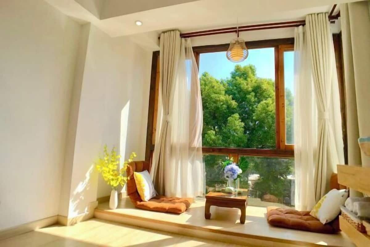 Une pièce avec une grande fenêtre, un canapé, une petite table et un vase rempli de fleurs.