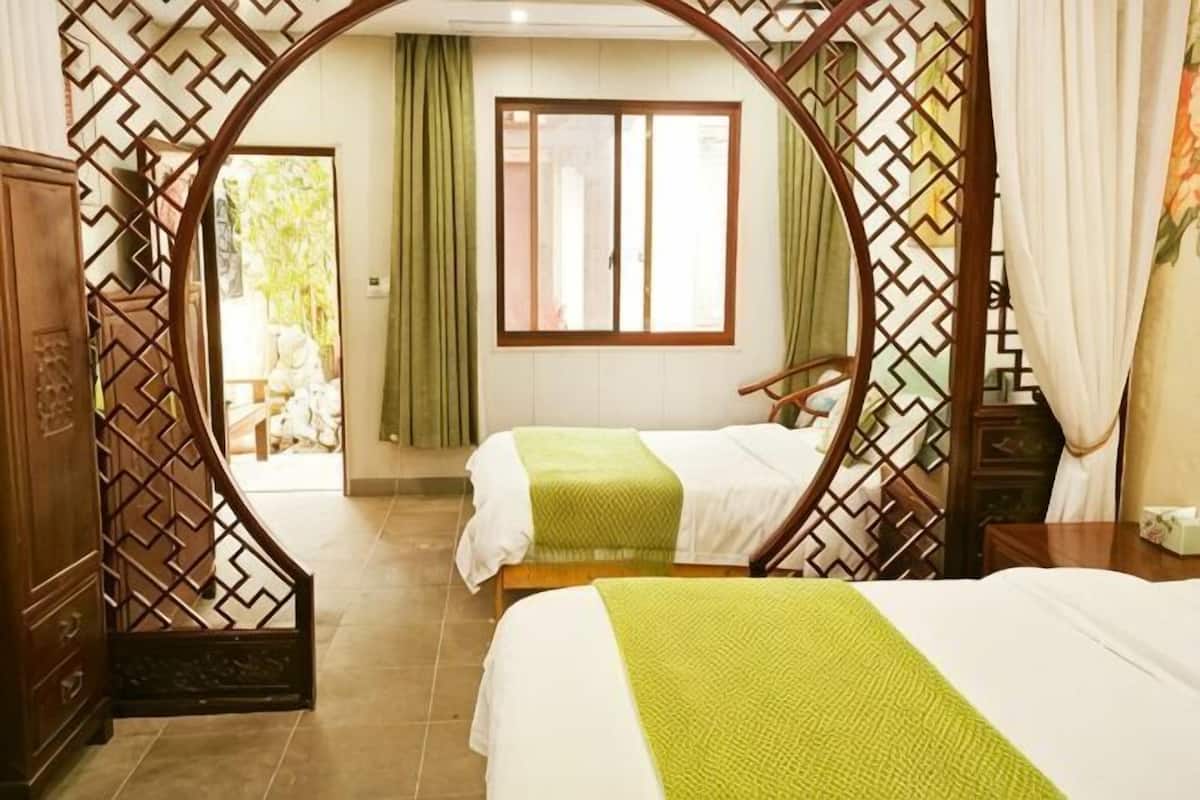 Une chambre avec deux lits, une cloison en bois, une fenêtre avec des rideaux et une vue sur l’extérieur.