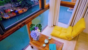 A room with a view of a river, a wooden table with a vase of flowers, a book, and a yellow cushion. - Shuishangju Japanese Landscape Inn Suzhou Tongli (Suzhou)