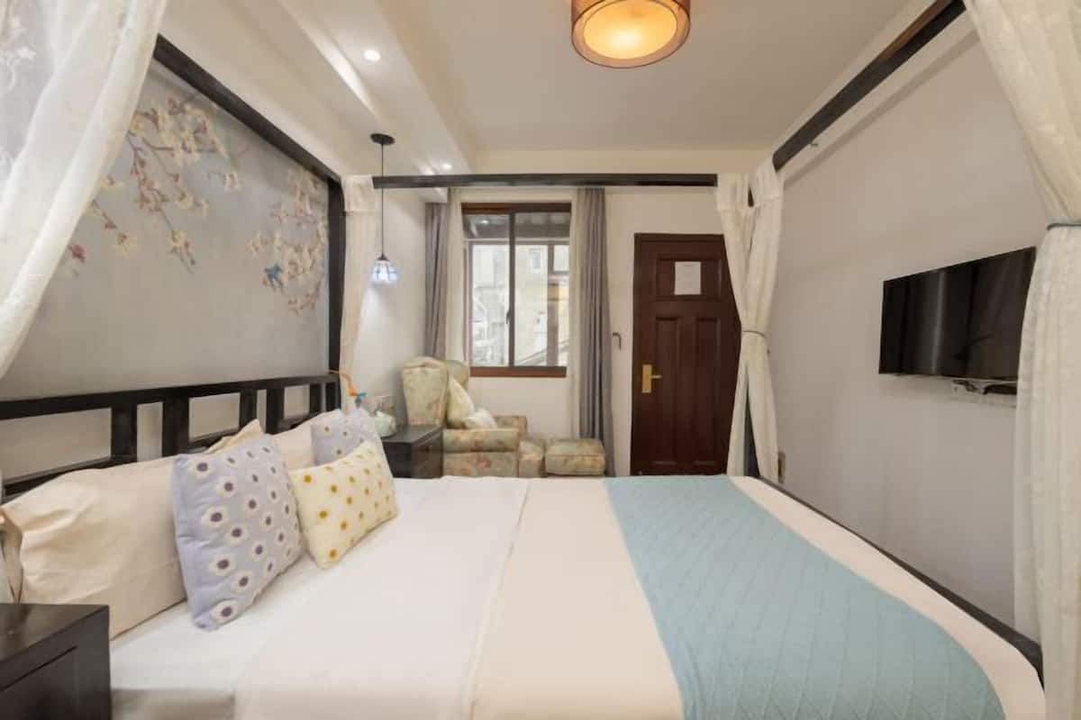 Une chambre à coucher avec un lit, des rideaux, une chaise, un téléviseur et une fenêtre.