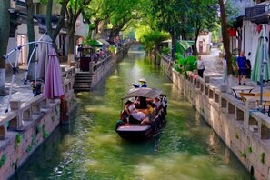 Un canal étroit où navigue un bateau transportant des passagers, avec des bâtiments de chaque côté et un pont en arrière-plan.