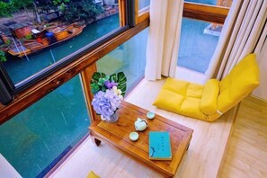 Una habitación con vistas a un canal, una mesa de madera con un jarrón y una tetera, y una silla con cojín amarillo.