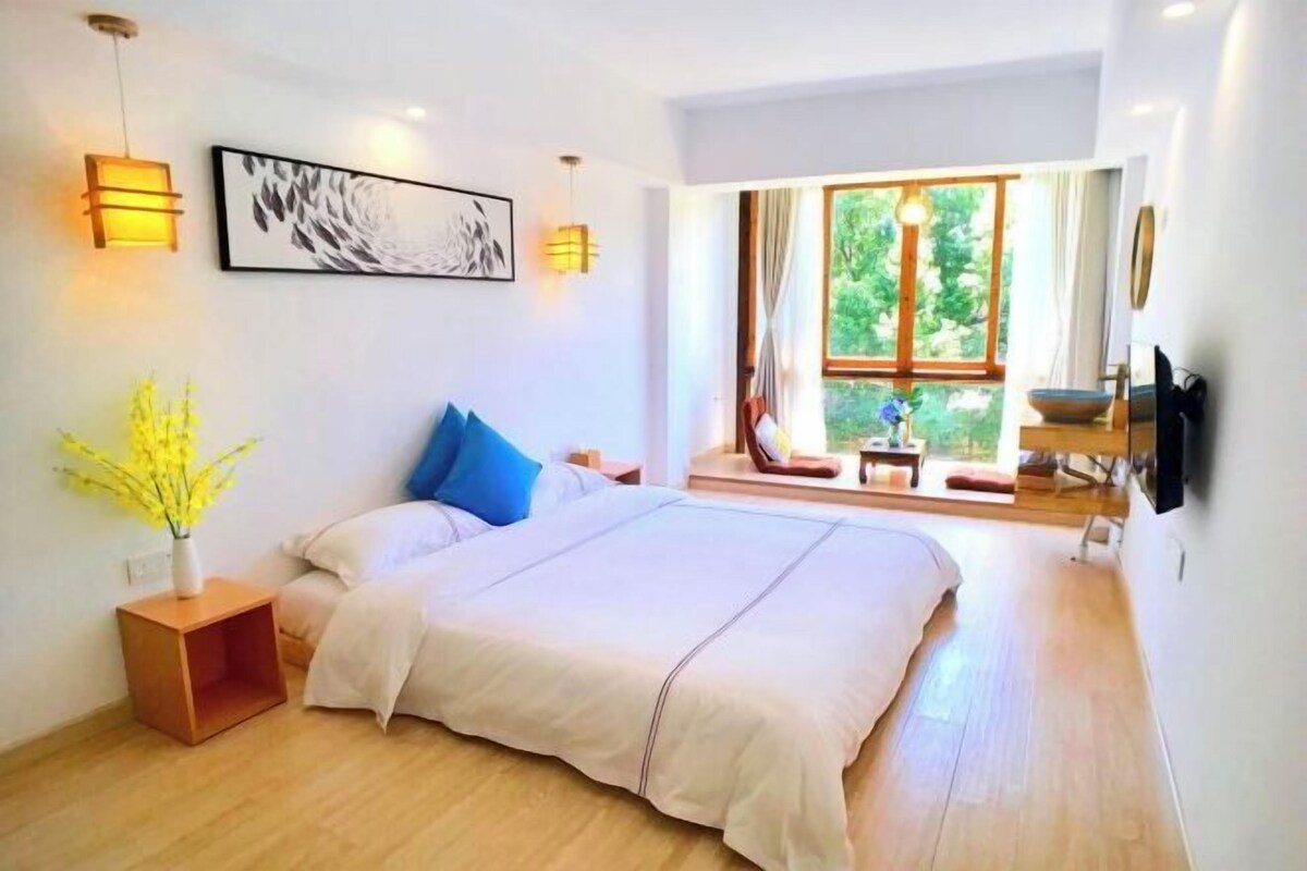 Un dormitorio moderno con una cama grande, lámparas de noche, una ventana con vistas y un cuadro en la pared.