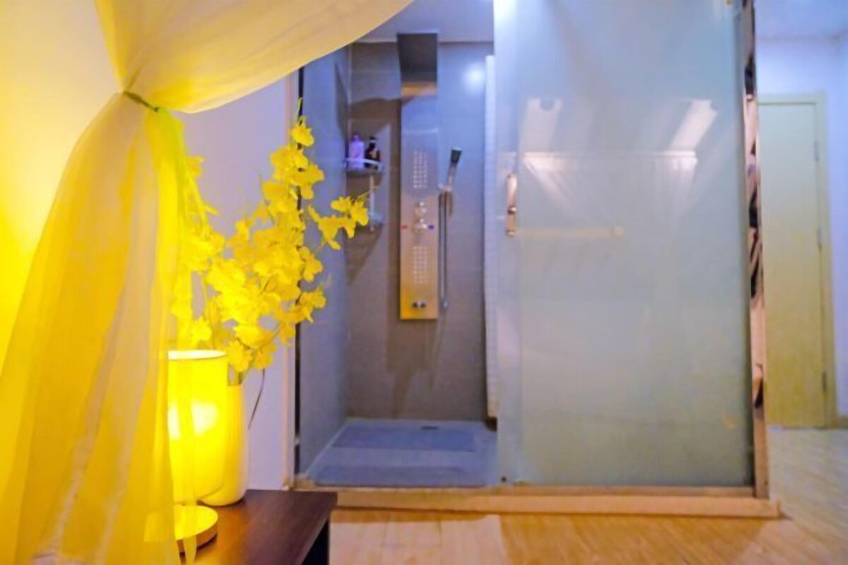 Habitación con cabina de ducha de vidrio, un banco de madera y un florero con flores amarillas.