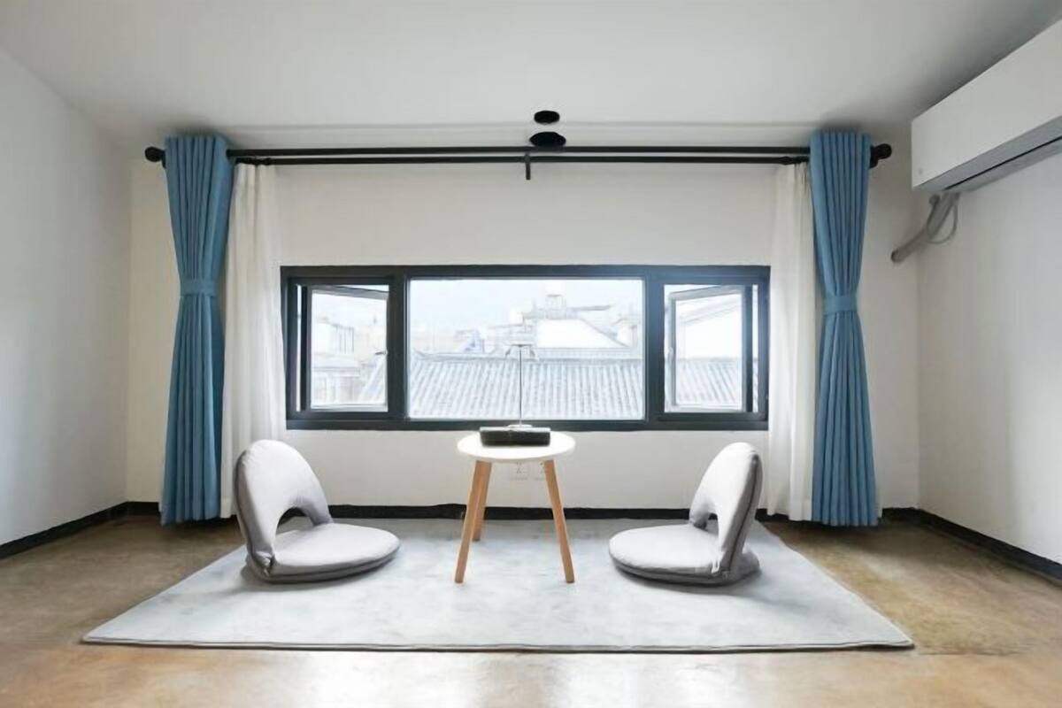 A room with a large window, two chairs, a small table, and a curtain rod.