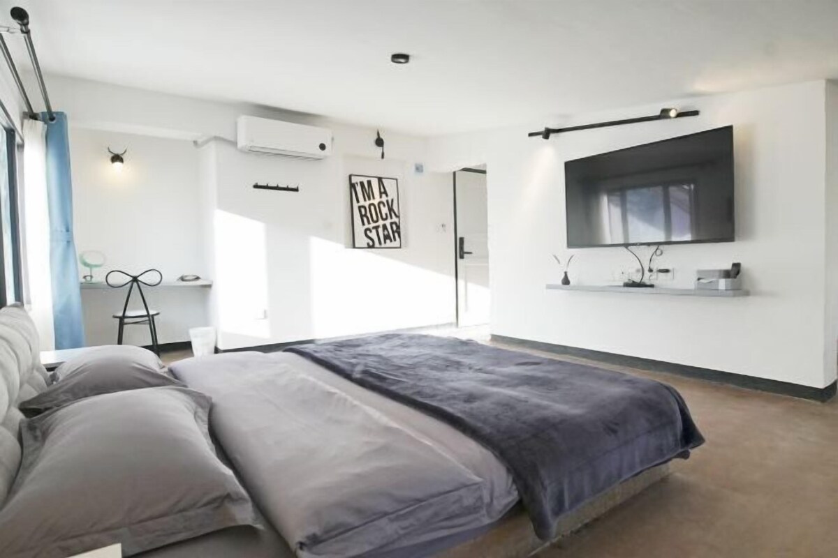 A modern bedroom with a bed, a desk, and a large window.
