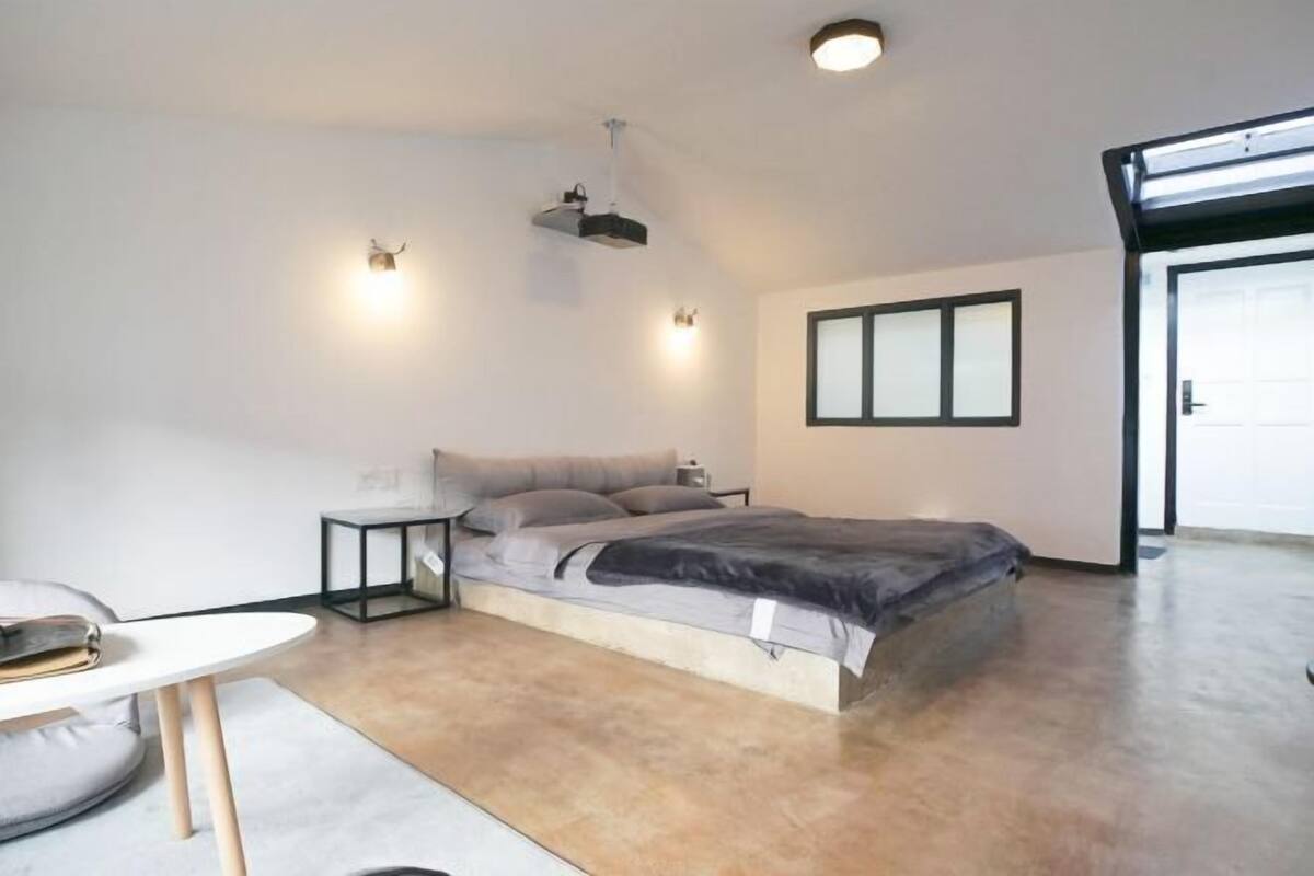 A modern bedroom with a bed, bedside tables, a small table, and a ceiling projector.