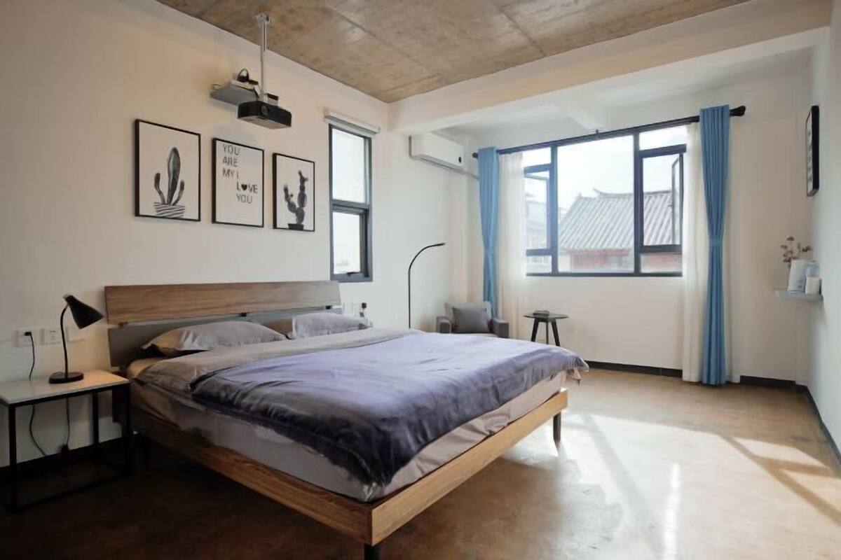 A bedroom with a bed, bedside tables, a window with curtains, and wall art.