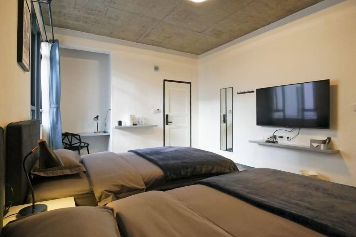 A modern hotel room with two beds, a desk, a chair, a TV, and a bathroom door.