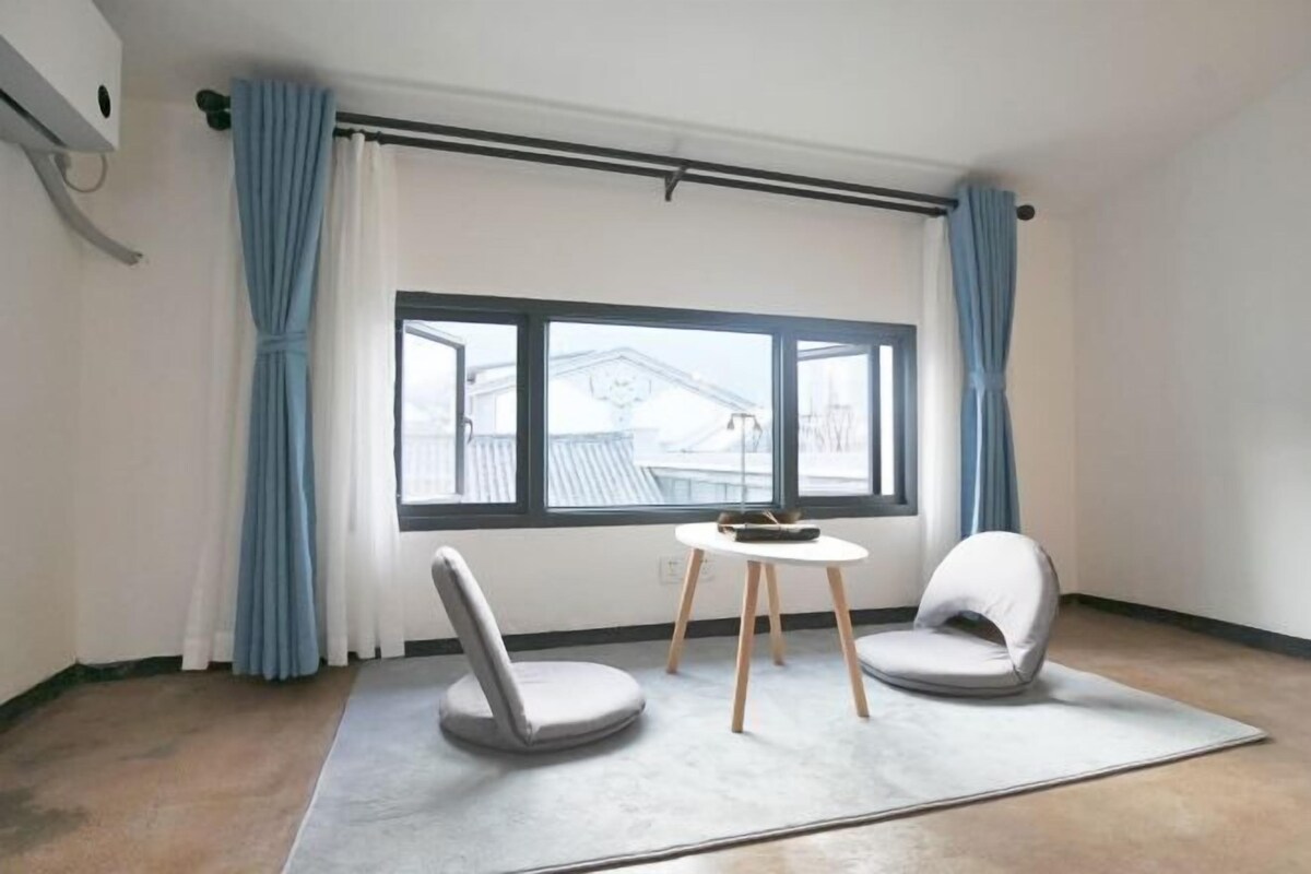 A room with a large window, two chairs, a small table, and a curtain rod.