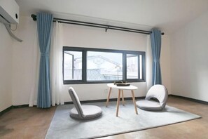 A room with a large window, two chairs, a small table, and a curtain rod.