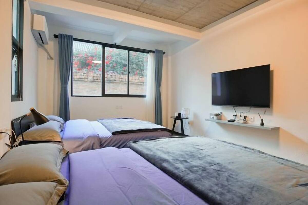 A hotel room with two beds, a TV, a small table, and a window with curtains.