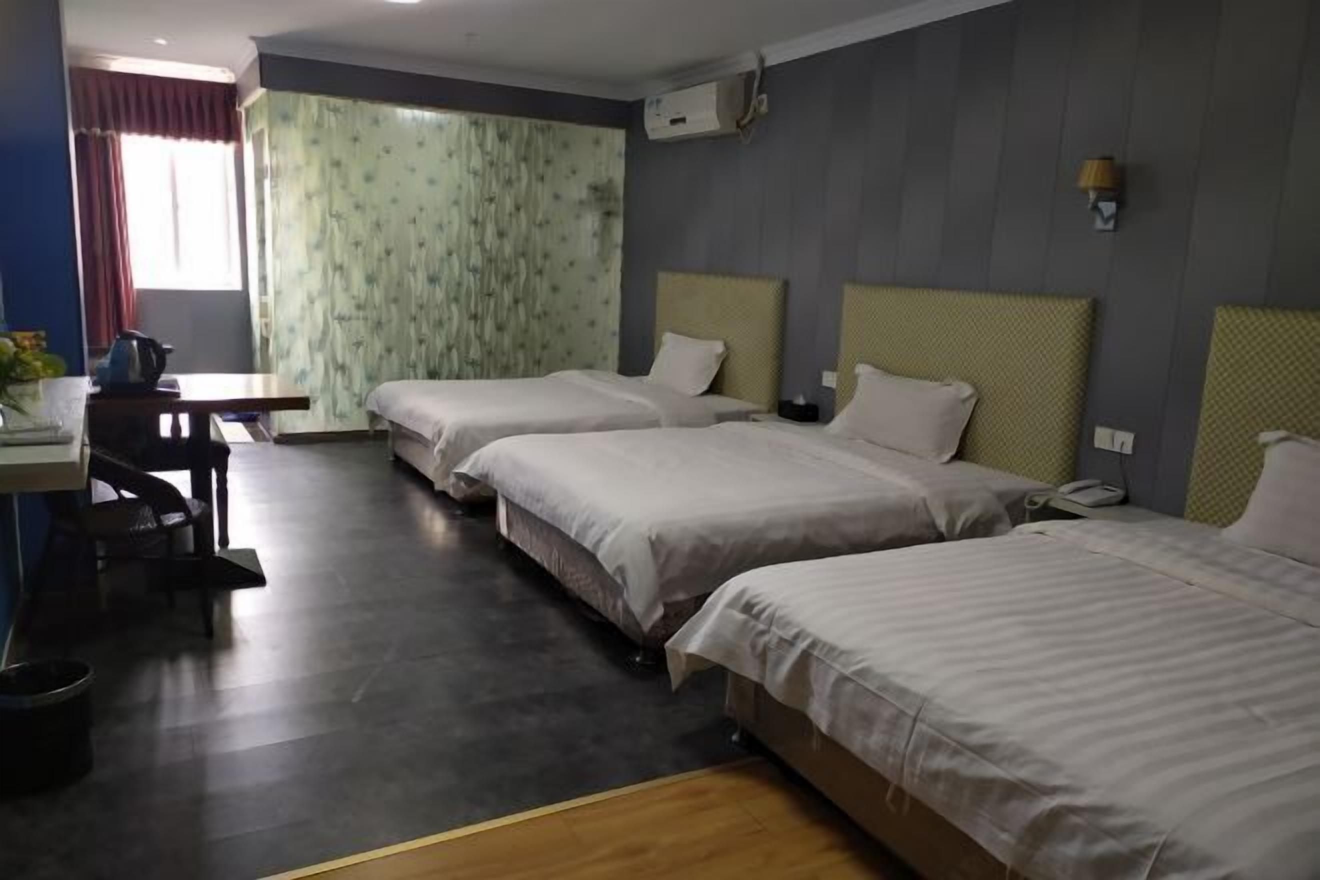 A hotel room with two single beds, a desk with a chair, a small table, and a window with curtains.