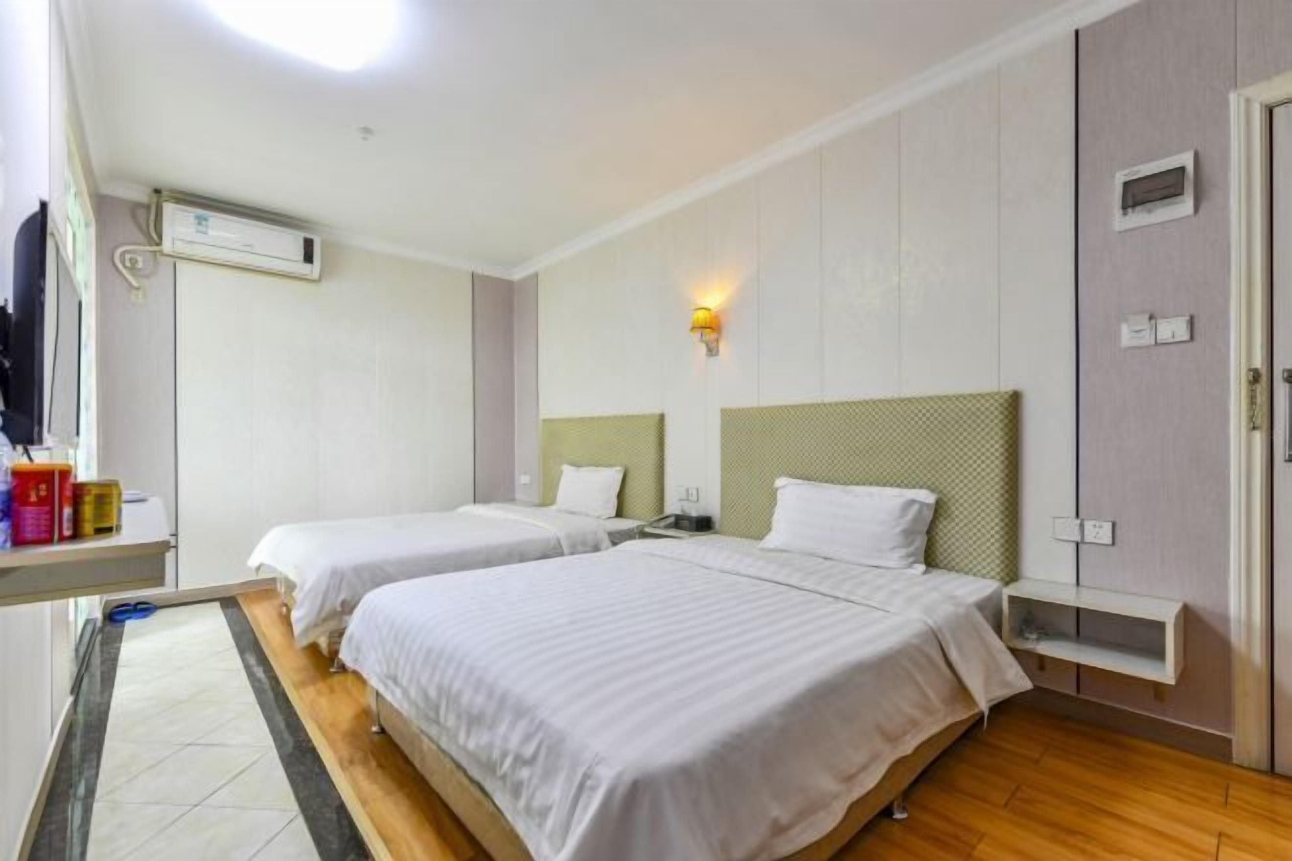 Hotellihuone, jossa on kaksi sänkyä, pieni työpöytä, seinään asennettu ilmastointilaite ja yöpöytälamppu.