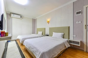 Een hotelkamer met twee bedden, een klein bureau, een wandairconditioner en een bedlampje.