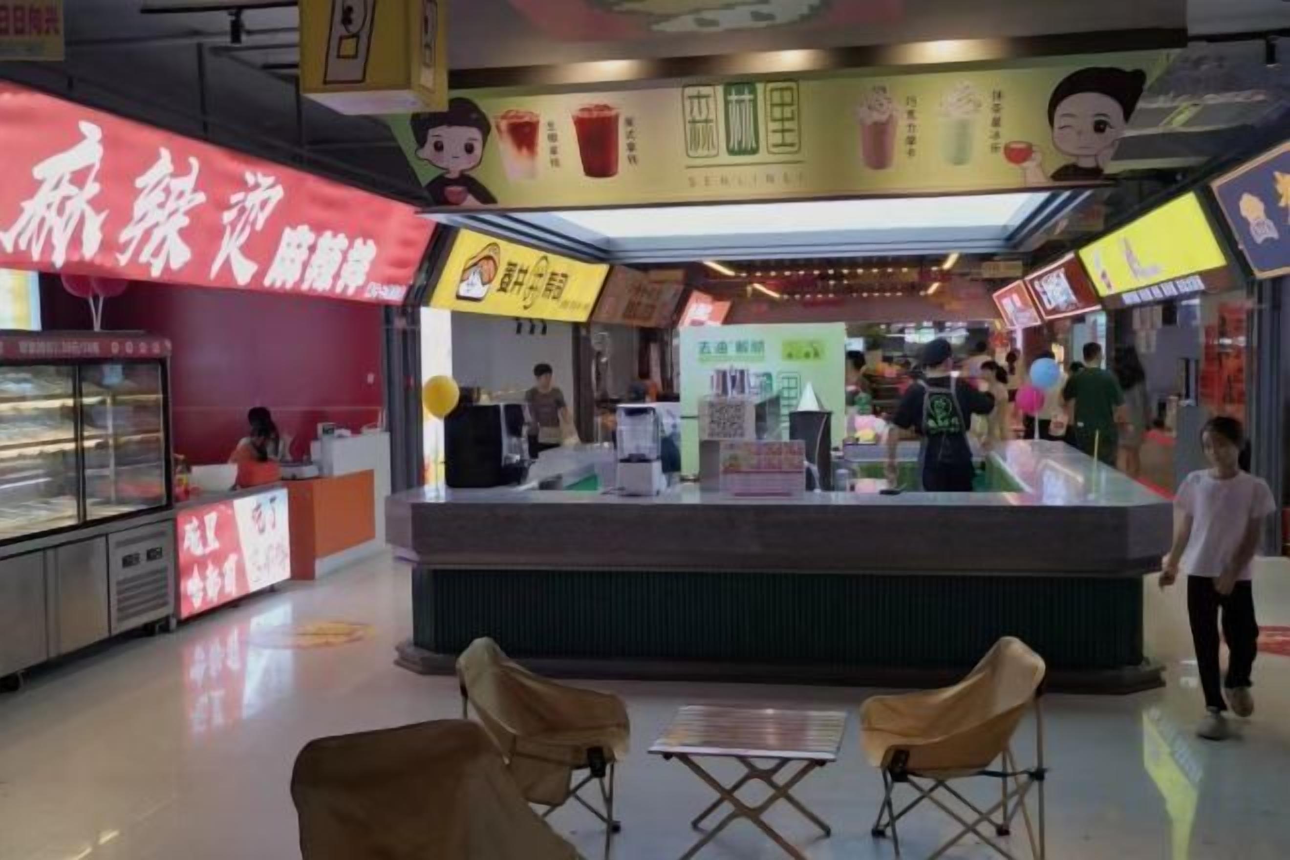 A food court with a counter, seating area, and a refrigerated display case.