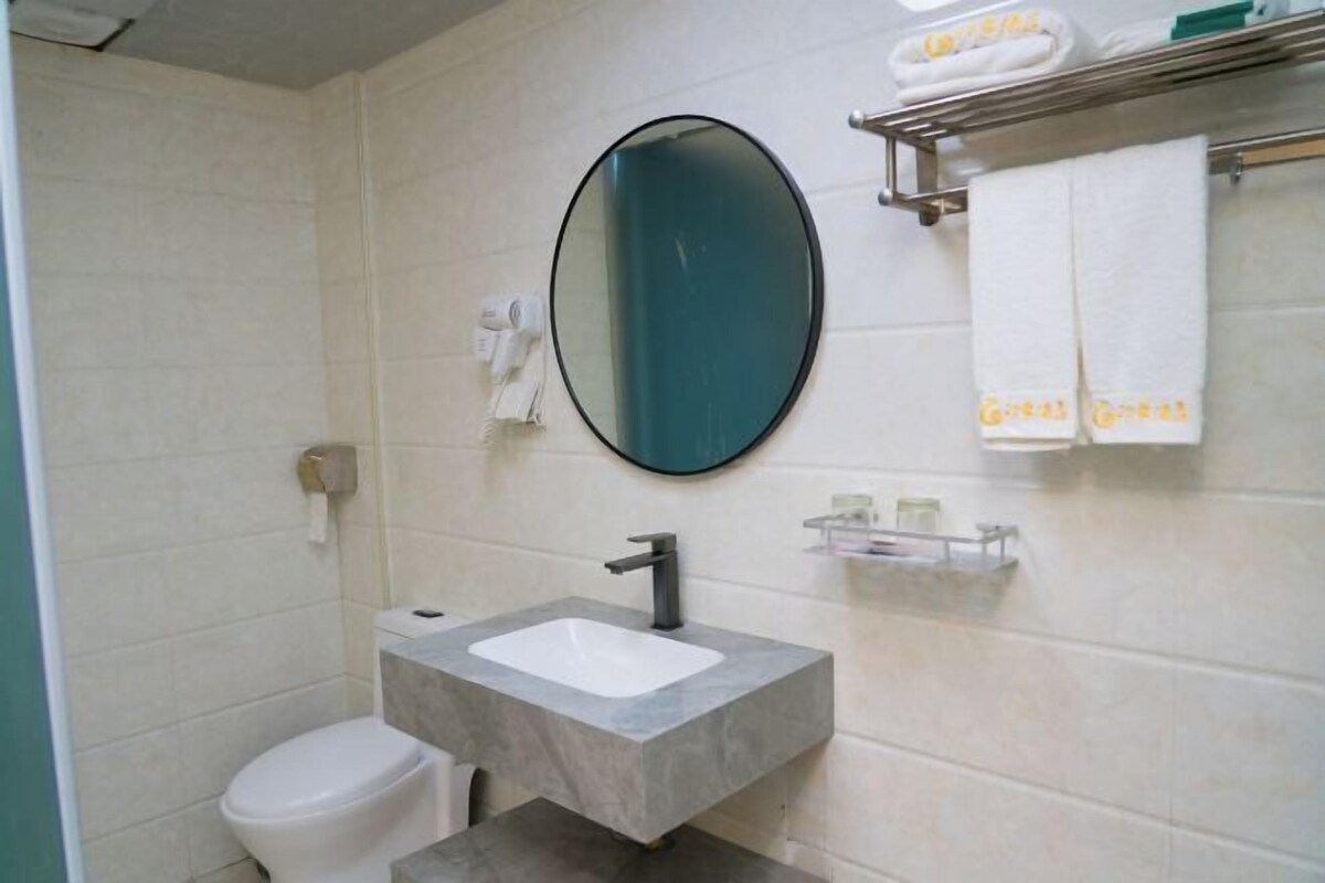 Een badkamer met een wit toilet, een rechthoekig wastafel met een zwarte kraan, een ronde spiegel en een handdoekrek met opgevouwen handdoeken.