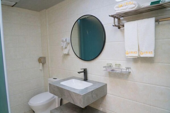 Een badkamer met een wit toilet, een rechthoekig wastafel met een zwarte kraan, een ronde spiegel en een handdoekrek met opgevouwen handdoeken.