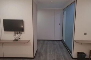Un couloir avec un téléviseur à écran plat fixé au mur, une poubelle et une porte donnant sur une autre pièce.