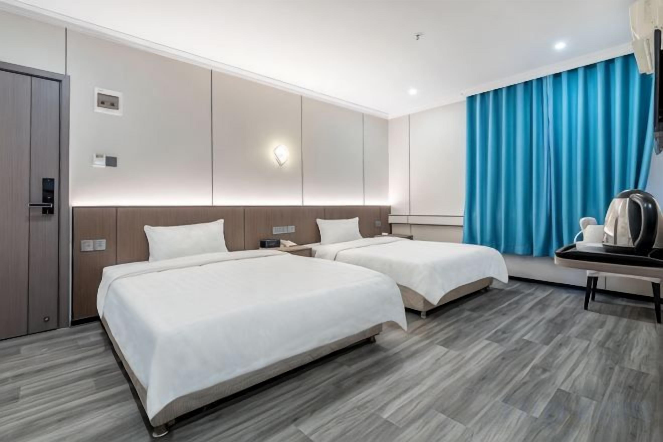 Ein Hotelzimmer mit zwei Betten, einem Schreibtisch, einer Kaffeemaschine und einem großen Fenster mit Vorhängen.