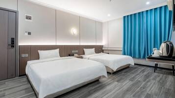 Ein Hotelzimmer mit zwei Betten, einem Schreibtisch, einer Kaffeemaschine und einem großen Fenster mit Vorhängen.