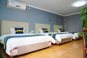 Een hotelkamer met twee bedden, elk met hoofdbord, wit beddengoed en deken in blauw-geel gestreept patroon.