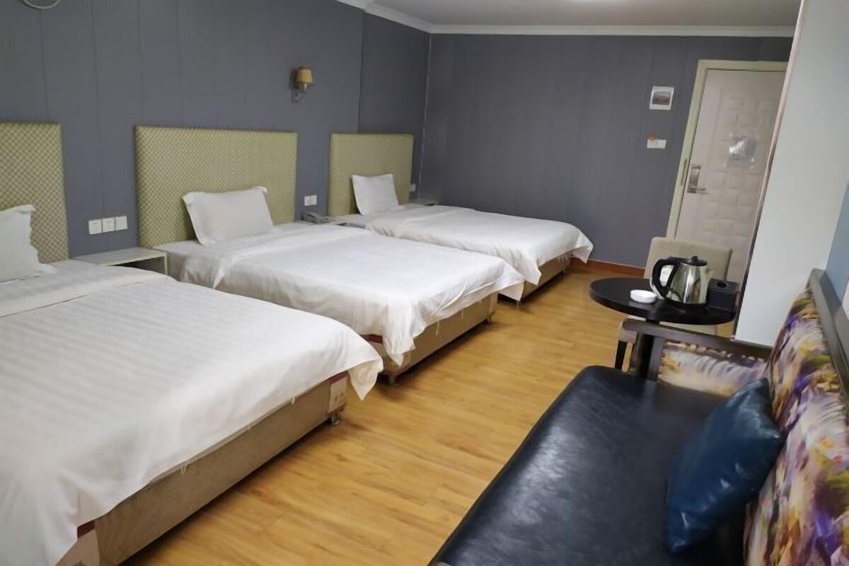 Een hotelkamer met drie enkele bedden, een klein tafeltje met een waterkoker en een bank.