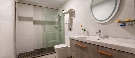 Un baño moderno con ducha de vidrio, inodoro, tocador con espejo y una pequeña estantería con flores.