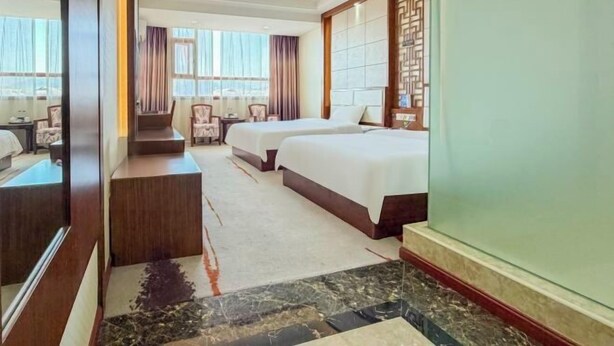 Una habitación de hotel con dos camas, un área de estar con una silla y una mesa, y un espejo grande.