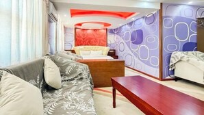 Una habitación de hotel moderna con sofá, una mesita de madera y una cama con una pared de acento roja.