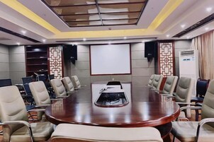 Uma sala de conferências com uma grande mesa oval, várias cadeiras, uma tela de projetor e um quadro branco.