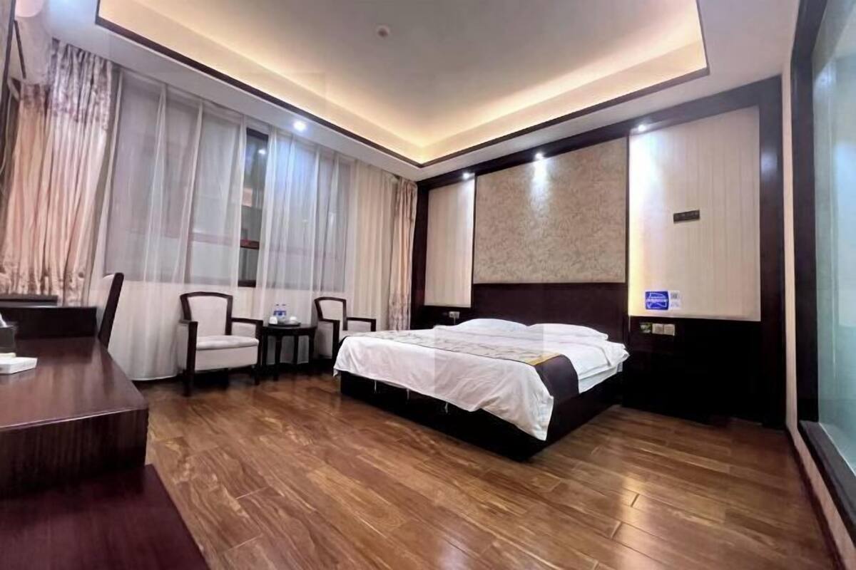 Hotellihuone, jossa on suuri sänky, työpöytä, kaksi tuolia ja ikkunasta avautuva näkymä ulos ohuen verhon läpi.
