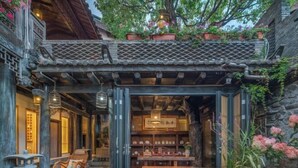 A traditional courtyard with a wooden table and chairs, surrounded by stone walls and potted plants. - Ten Courtyard Inn (Lijiang)