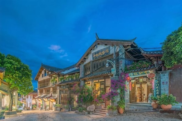 A traditional building with a sign, potted plants, and a cobblestone street.