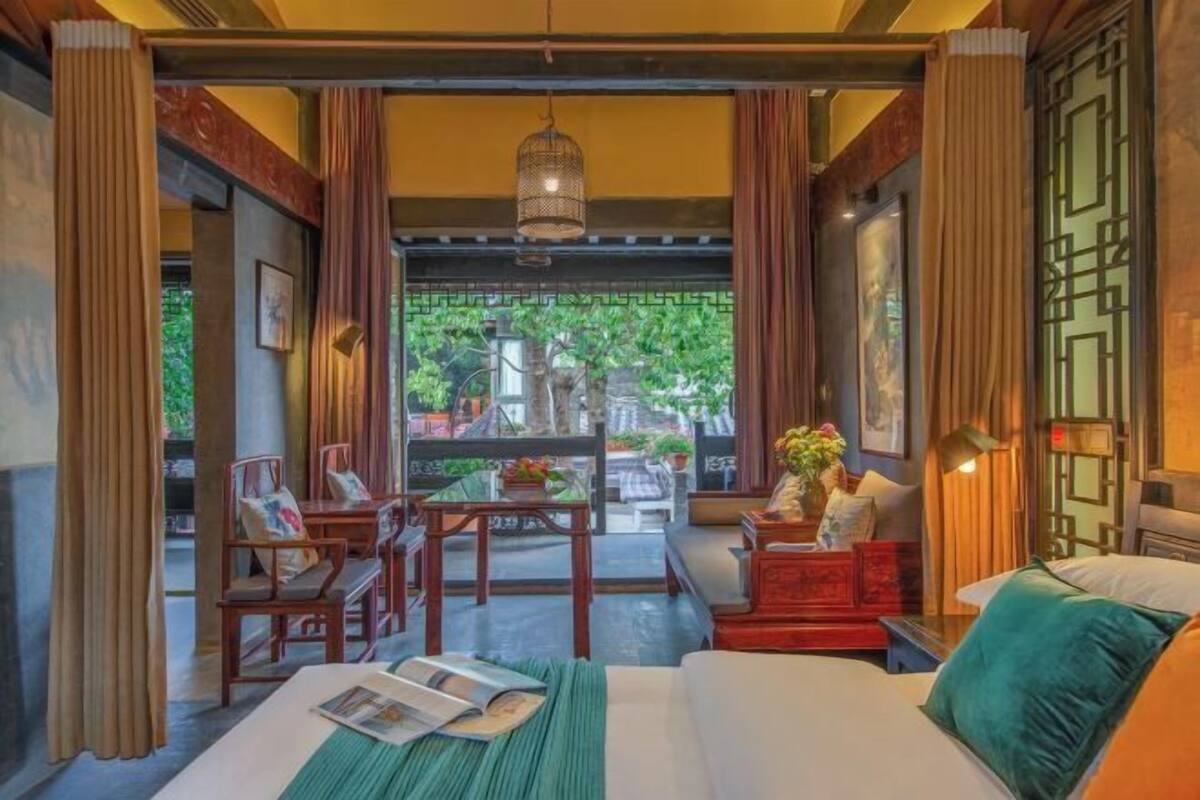 A hotel room with a bed, a table with chairs, a sofa, and a view of greenery outside.