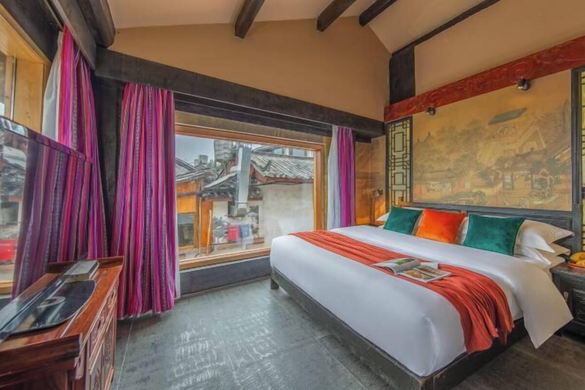 A hotel room with a bed, curtains, a window, a desk, and a wall with a painting.