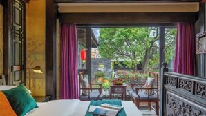 A hotel room with a bed, a small table, two chairs, and a view of a garden through a glass door. - Ten Courtyard Inn (Lijiang)