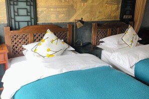 A room with two beds, a wooden headboard, a wall with a geometric pattern, and a small table with a lamp. - Ten Courtyard Inn (Lijiang)