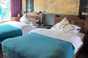 A hotel room with two beds, each with a blue bedspread and white pillows, a wooden headboard, a nightstand, and a wall with a traditional design. - Ten Courtyard Inn (Lijiang)